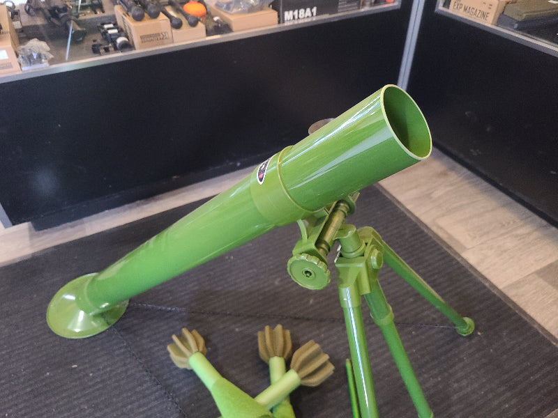 Green airsoft mortar with adjustable bipod stand displayed on black mat indoors