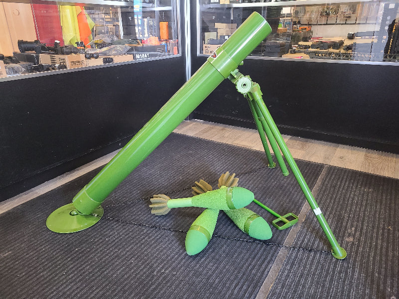 Green airsoft mortar with three matching green mortar shells displayed indoors on black carpet