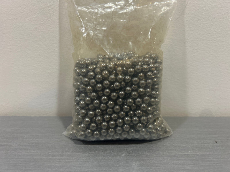 Clear plastic bag of silver 6mm steel BBs for airsoft on gray tabletop against white wall
