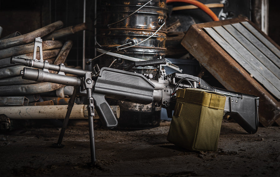 High quality Airsoft LMG replica with bipod and ammo pouch in a rustic airsoft gear setting
