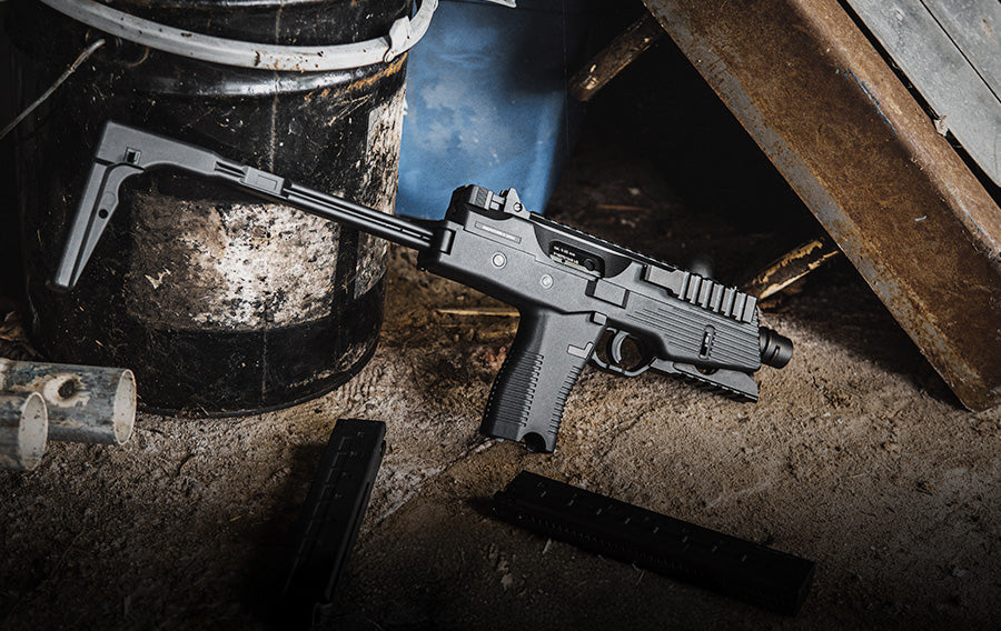 Person aiming a tactical Airsoft SMG with suppressor and optic in outdoor combat simulation